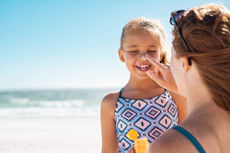 mom putting sunscreen on daughter at beach