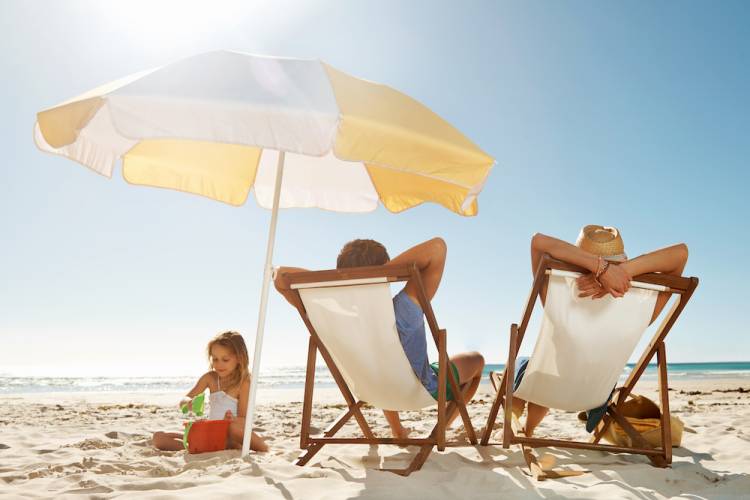 couple in beach chairs with umbrella overhead and kid playing in sand